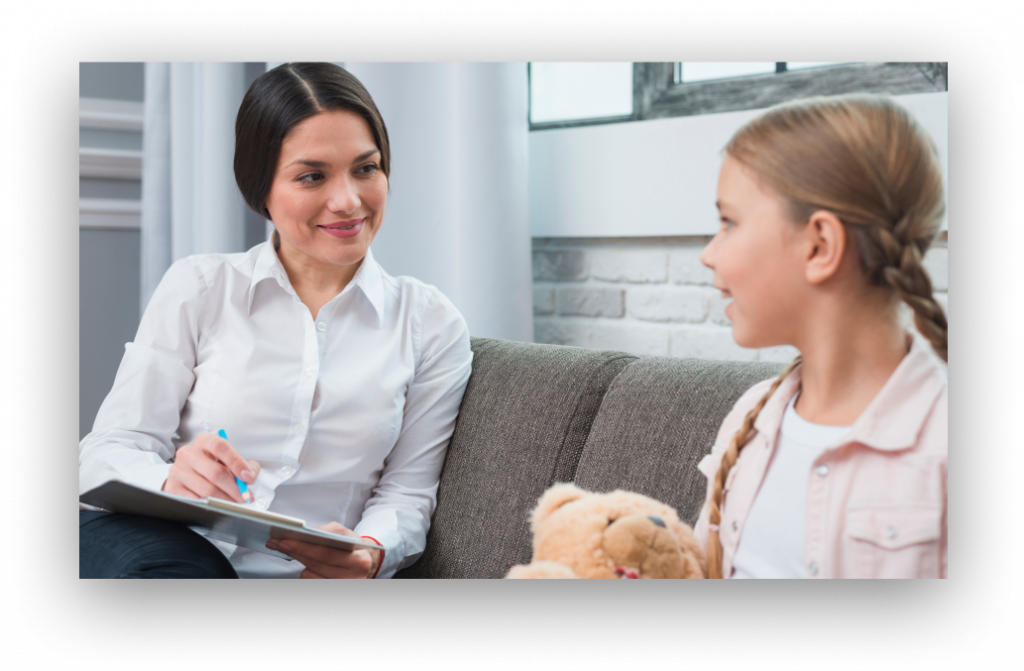 Therapist with clipboard smiling at a girl on a couch during a counseling session with a teddy bear nearby